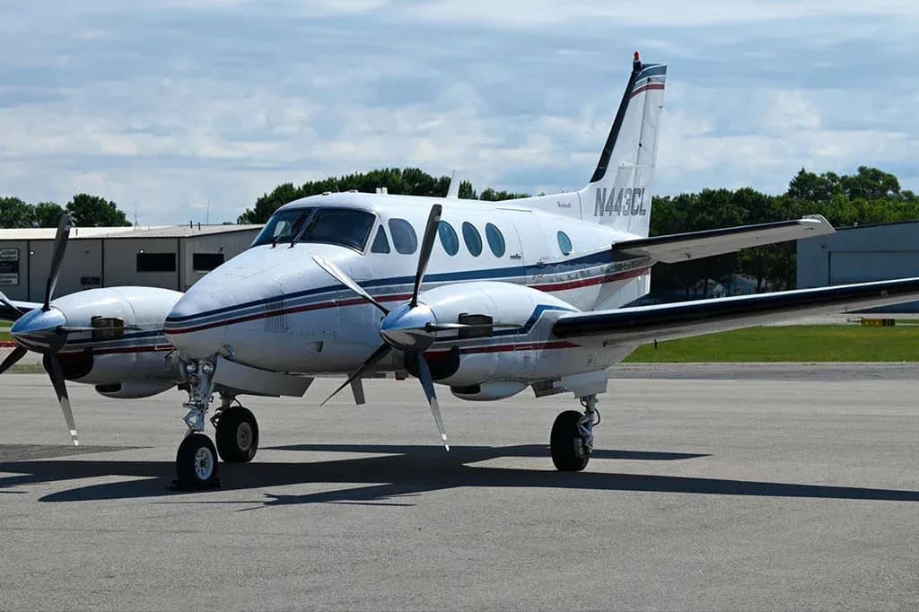 A three-quarter front view of a white Beechcraft King Air C90GTx with blue and red stripes, parked on the tarmac.