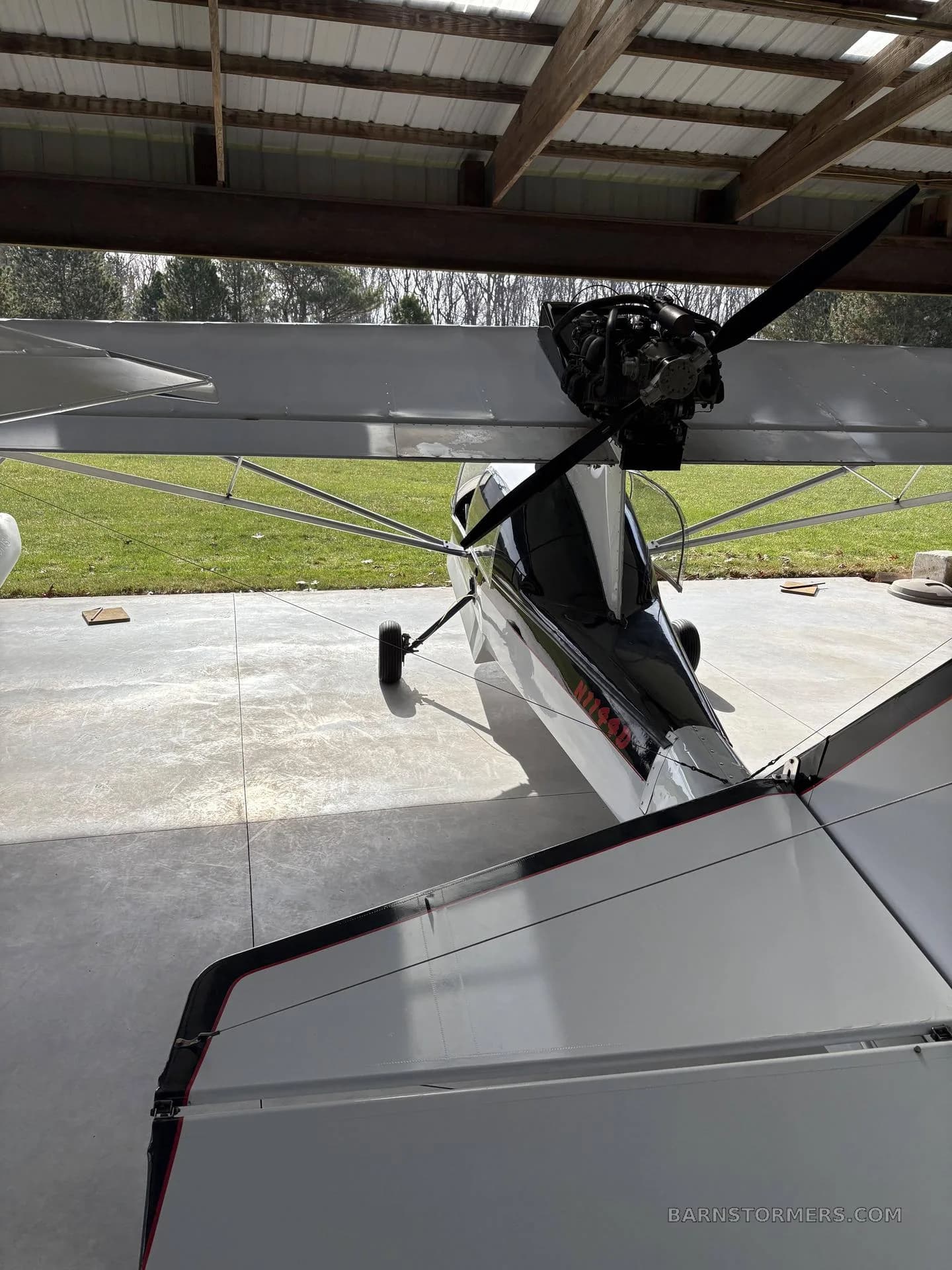 A rear view of a white and black ultralight aircraft with registration N7749D parked inside a hangar.
