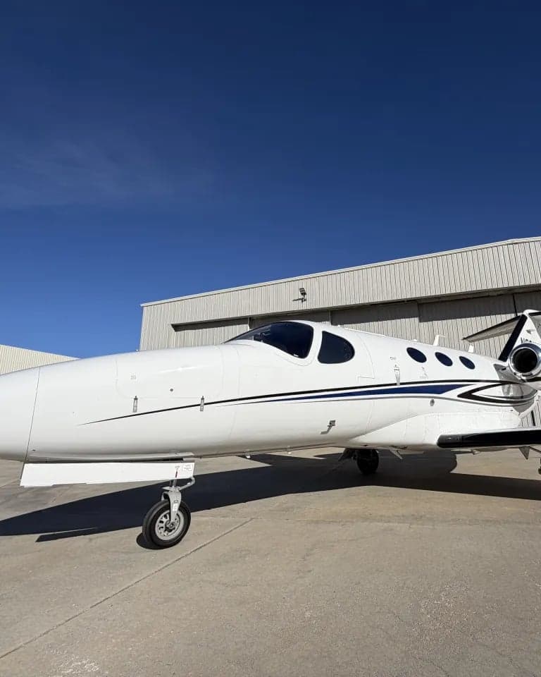 A Citation Mustang aircraft parked on the tarmac in front of a hangar.