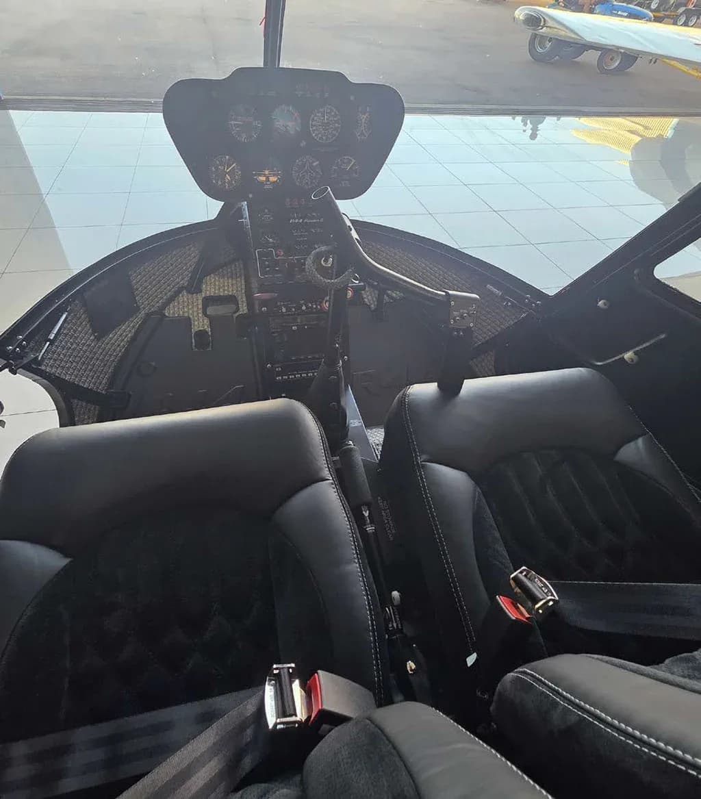 A front view of the helicopter cockpit showing the instrument panel and two black quilted seats.
