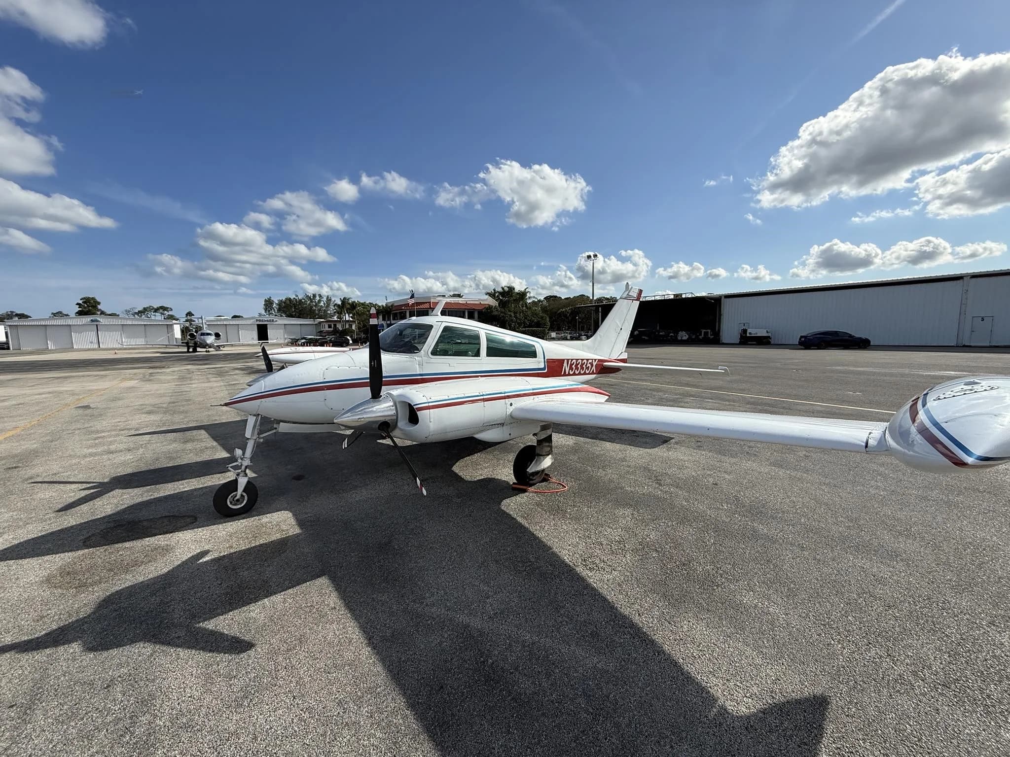 A white Cessna 310L with red and blue stripes parked on an airport tarmac, showing the right side.