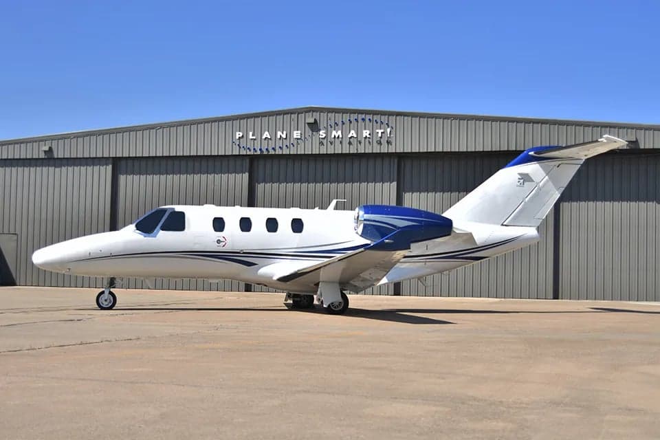 A Cessna Citation CJ3 is parked on the tarmac in front of a hangar.