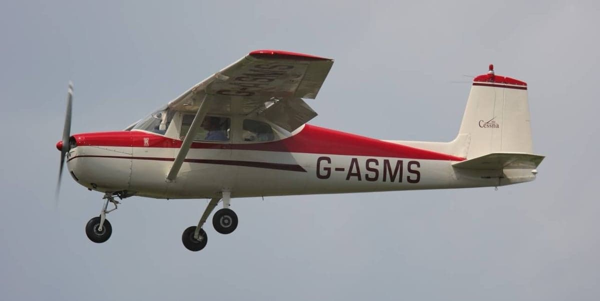 A white and red Cessna 150 G-ASMS in flight against a light blue sky.