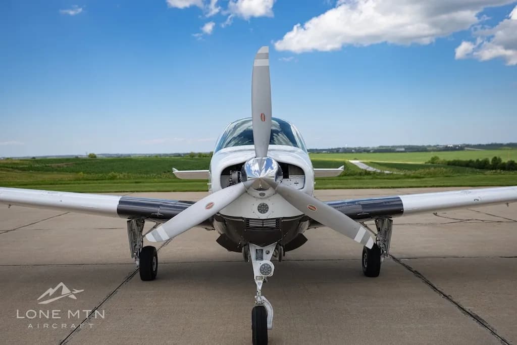 A front view of a white and dark grey Beechcraft Baron N85BB with its propeller centered, parked on a tarmac.