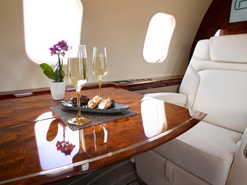 The aircraft's interior features a table with champagne glasses and snacks.