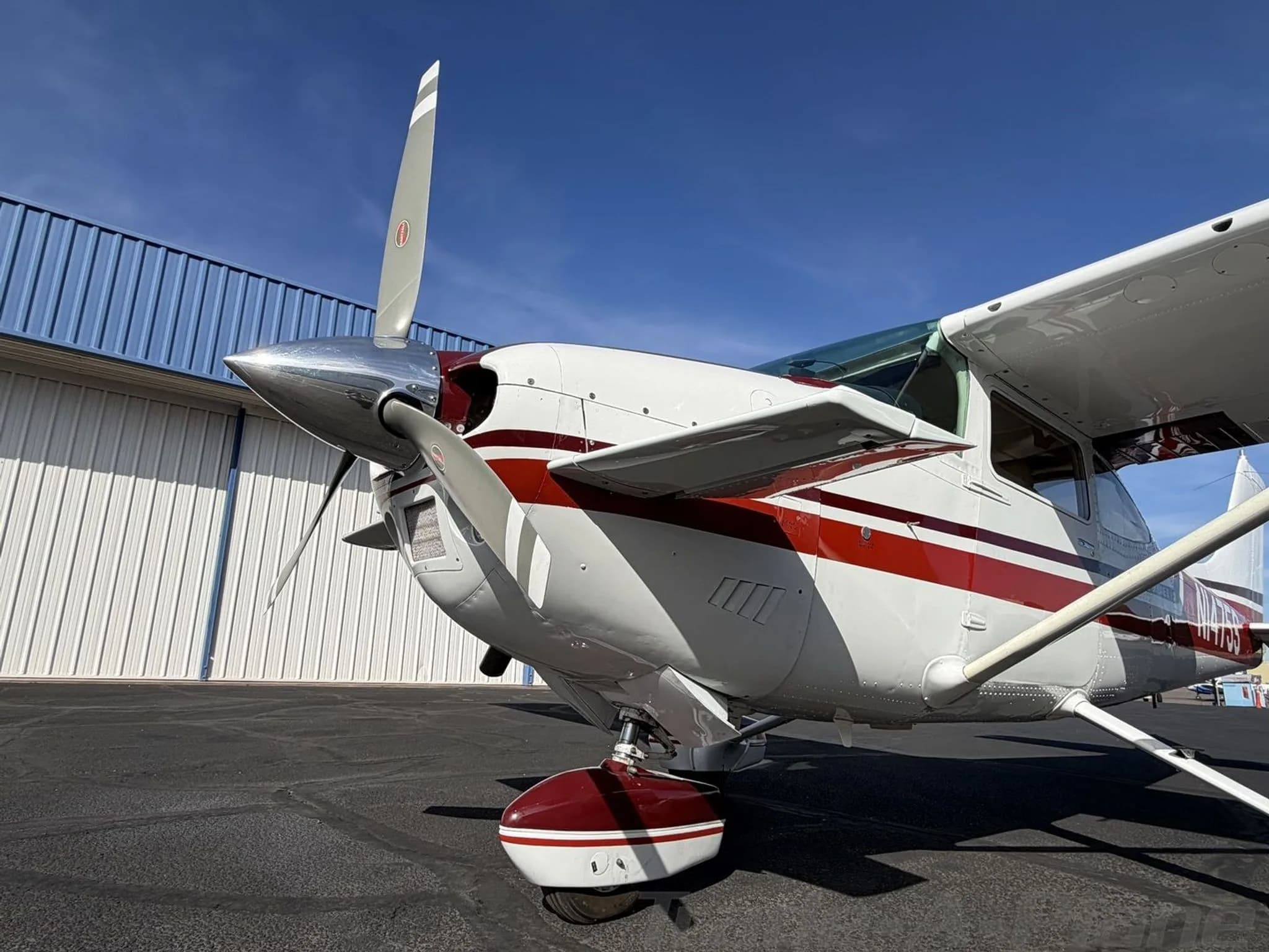 A low-angle front-left view of the propeller and landing gear of the white and red Cessna Skylane II.