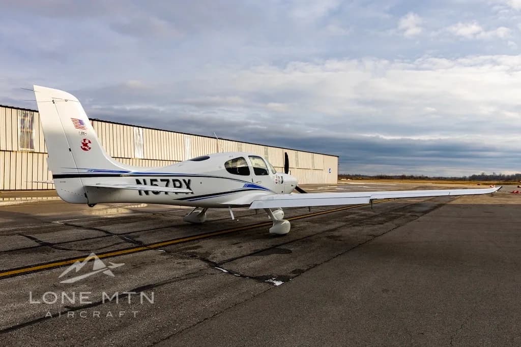 A rear-side view of a white Cirrus SR22 aircraft with blue and black stripes, tail number N57PX, parked on an airport tarmac.