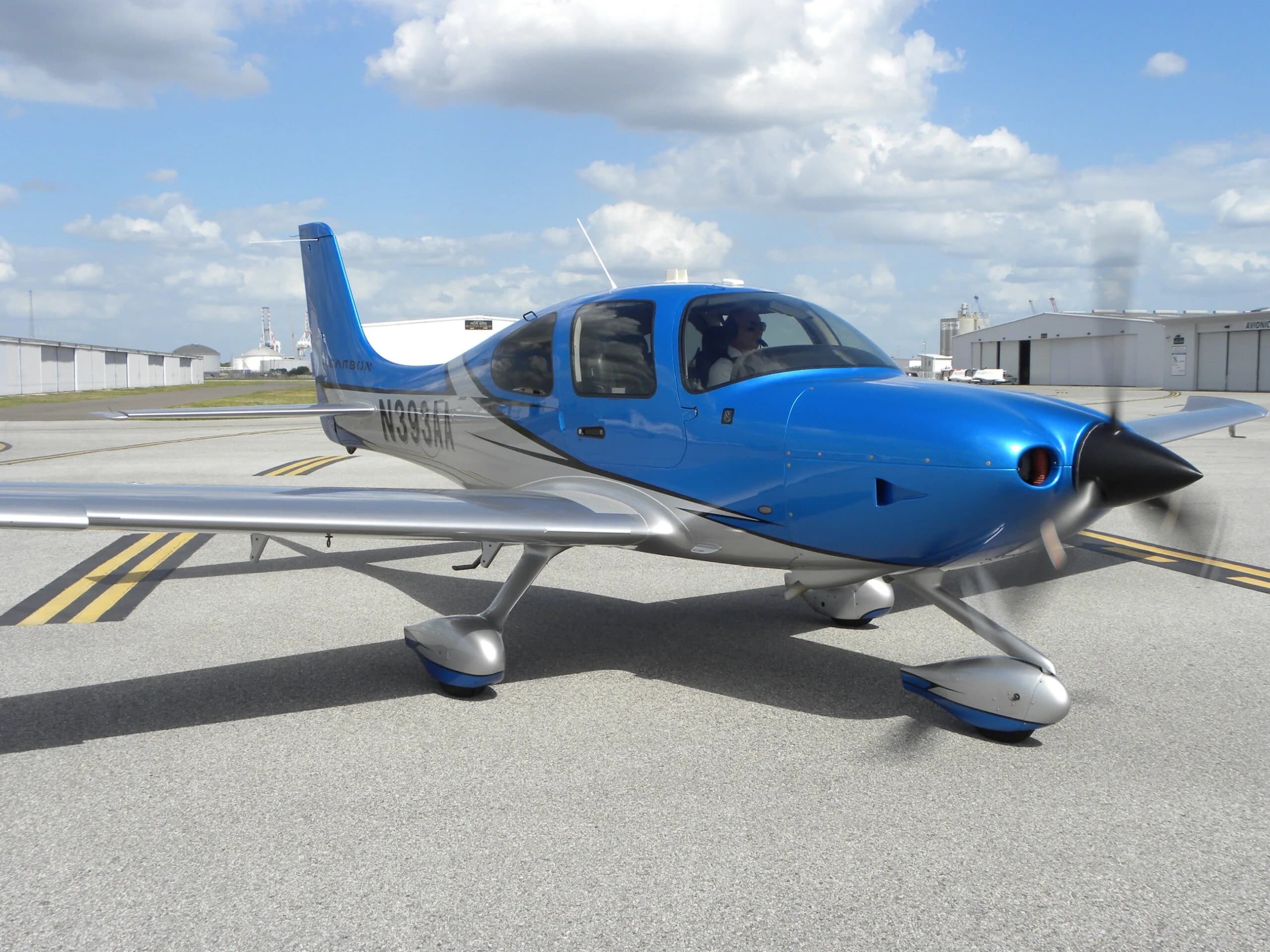 A blue and silver Cirrus SR22 aircraft with registration N393AA, parked on an asphalt ramp with its propeller spinning.