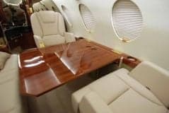 The aircraft's interior features a wooden table and cream-colored leather seats.