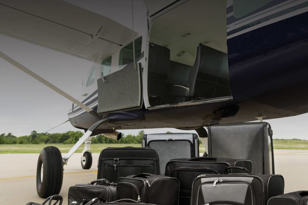 Luggage piled in front of a Cessna Caravan with open doors.
