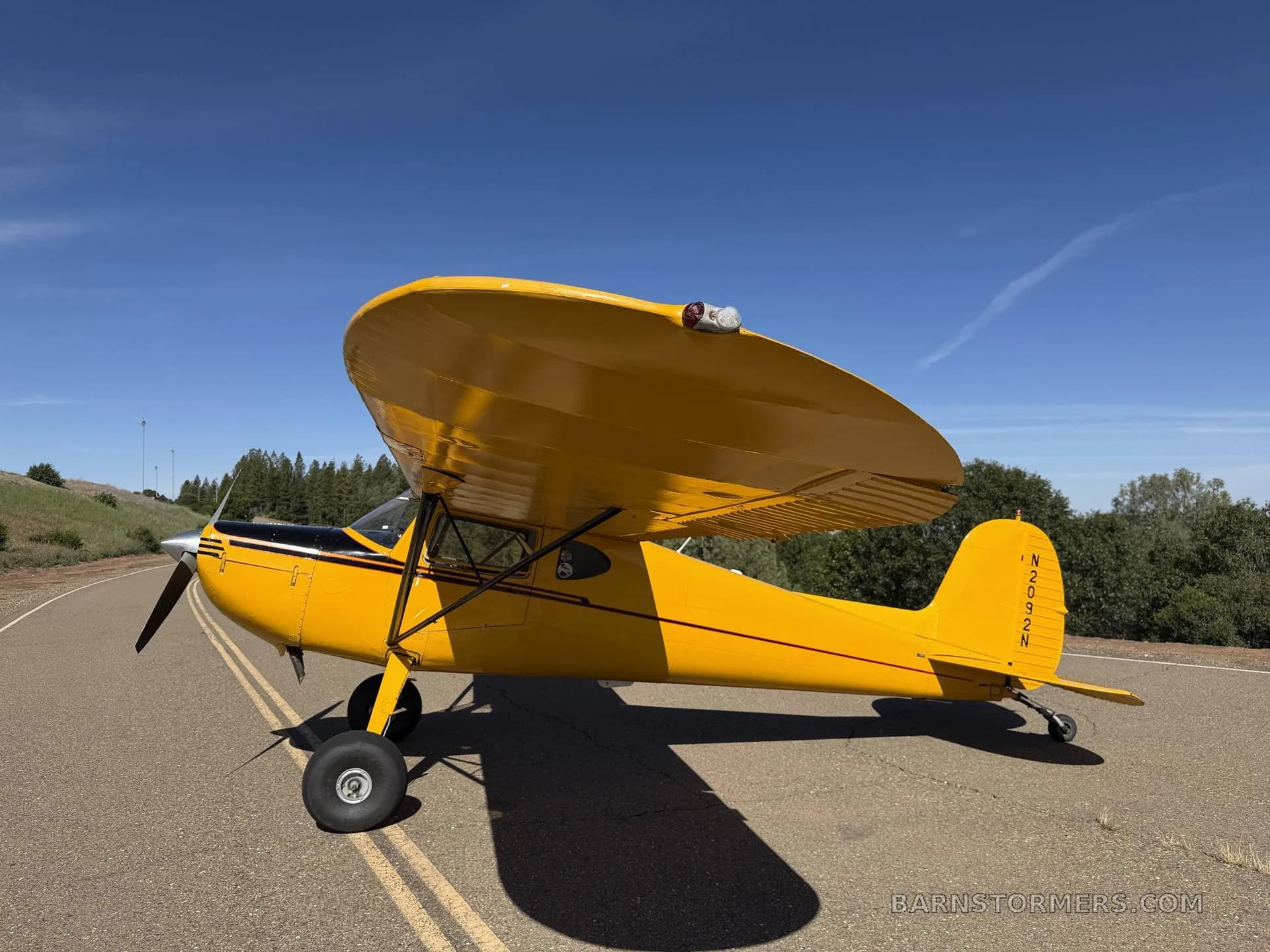 A bright yellow high-wing monoplane aircraft, N2092N, is parked on an asphalt surface under a clear blue sky, viewed from the front-left side.