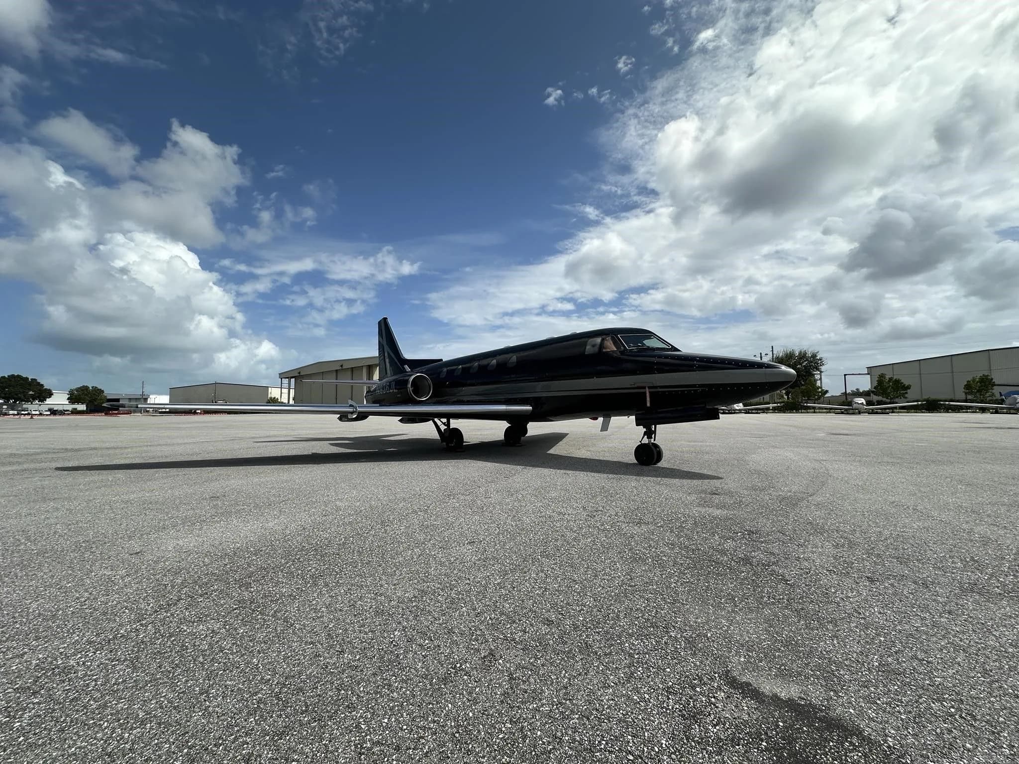 A wide-angle front-side view of a black and silver business jet parked on a large asphalt tarmac.