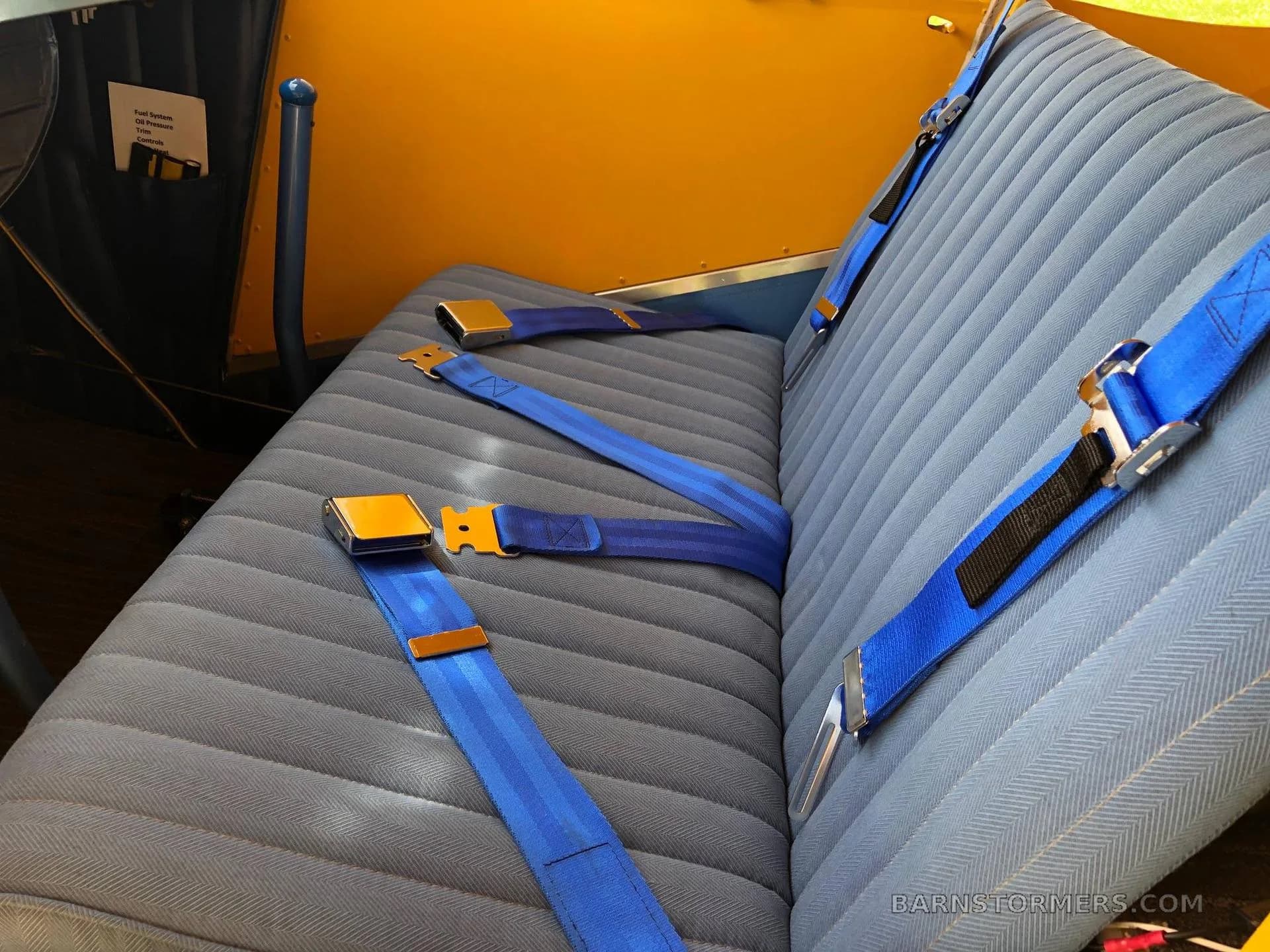 The blue fabric seats with blue seatbelts inside a yellow aircraft cabin.