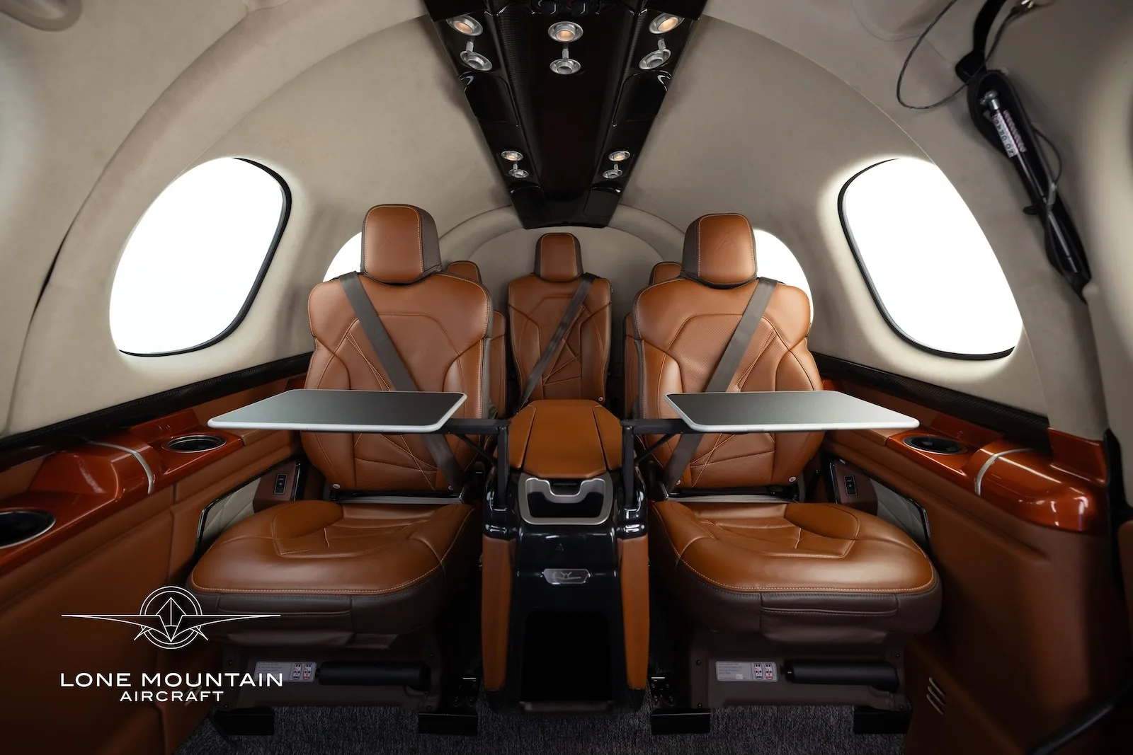 The brown leather interior cabin of a Cirrus Vision Jet (SF50) showing passenger seats with fold-out tables.