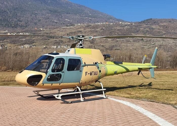 Side view of a tan and green Eurocopter AS350 helicopter parked on a helipad.