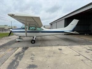 Side view of a Cessna aircraft with a white and blue paint scheme parked on the tarmac.
