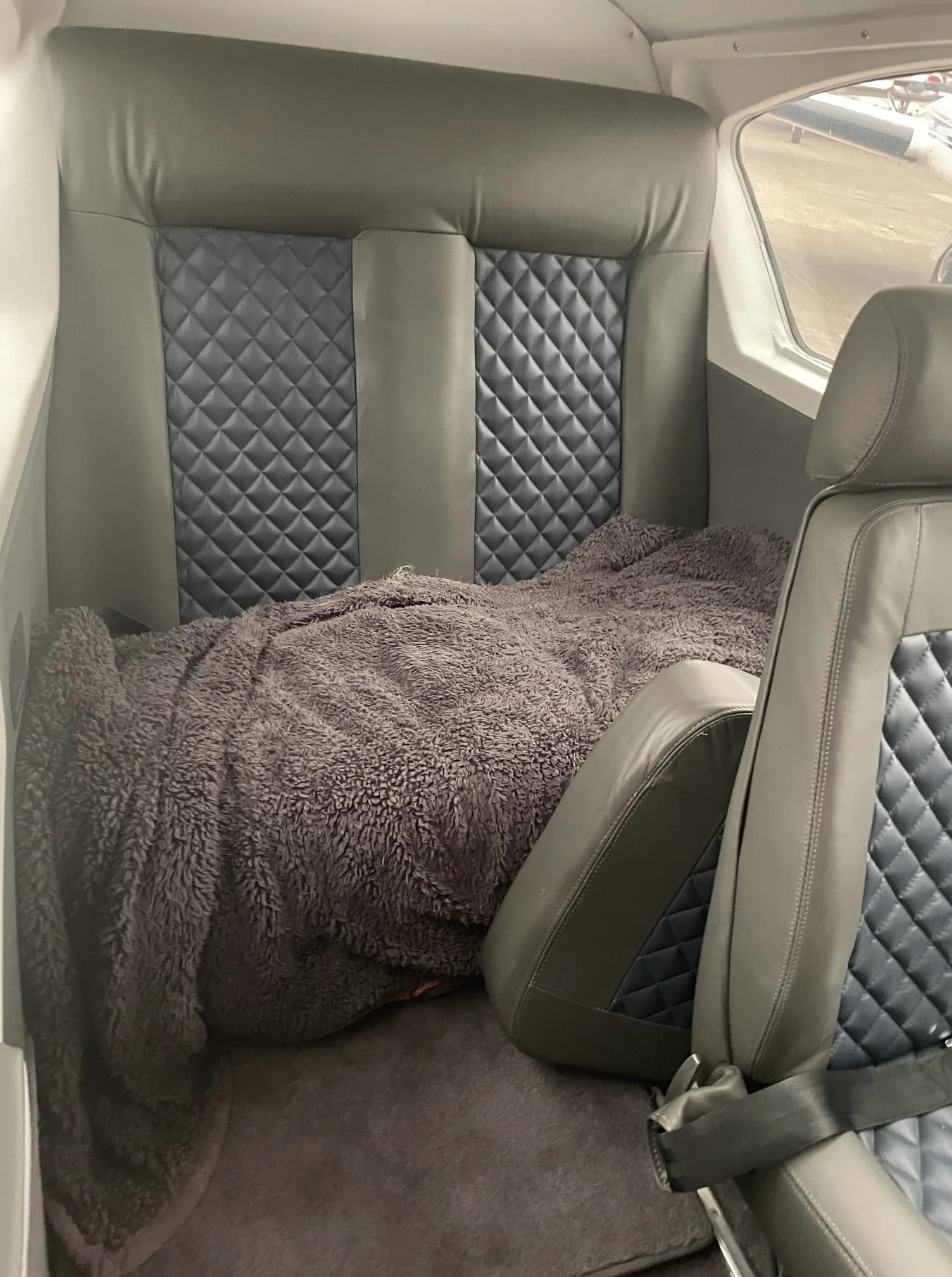 The aircraft's cabin interior with grey and blue quilted leather seats, one covered by a blanket.