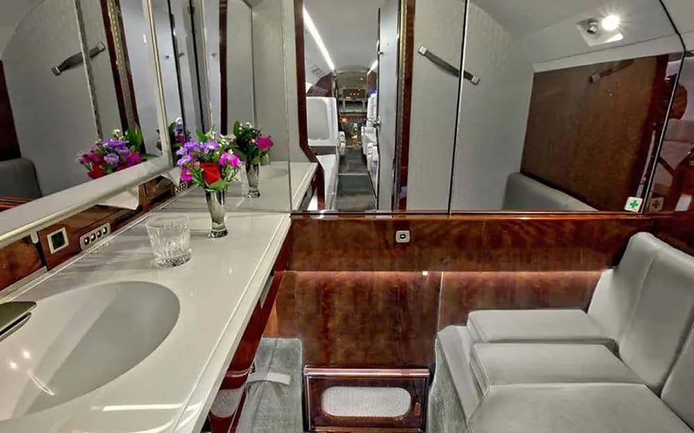 The lavatory or vanity area of a business jet featuring a sink, mirror, and floral arrangement.