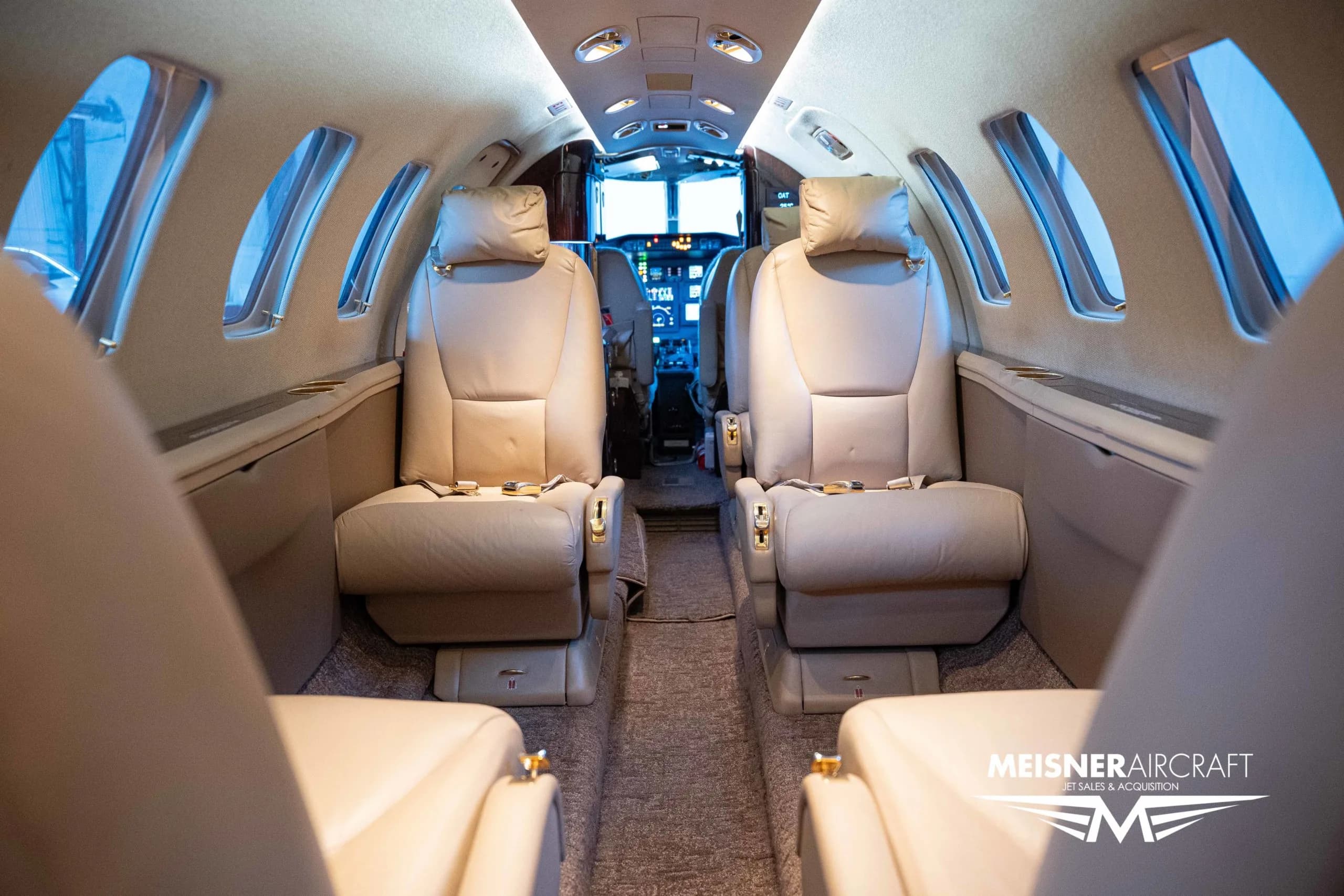The interior cabin of a private jet, featuring beige leather seats, looking towards the cockpit.