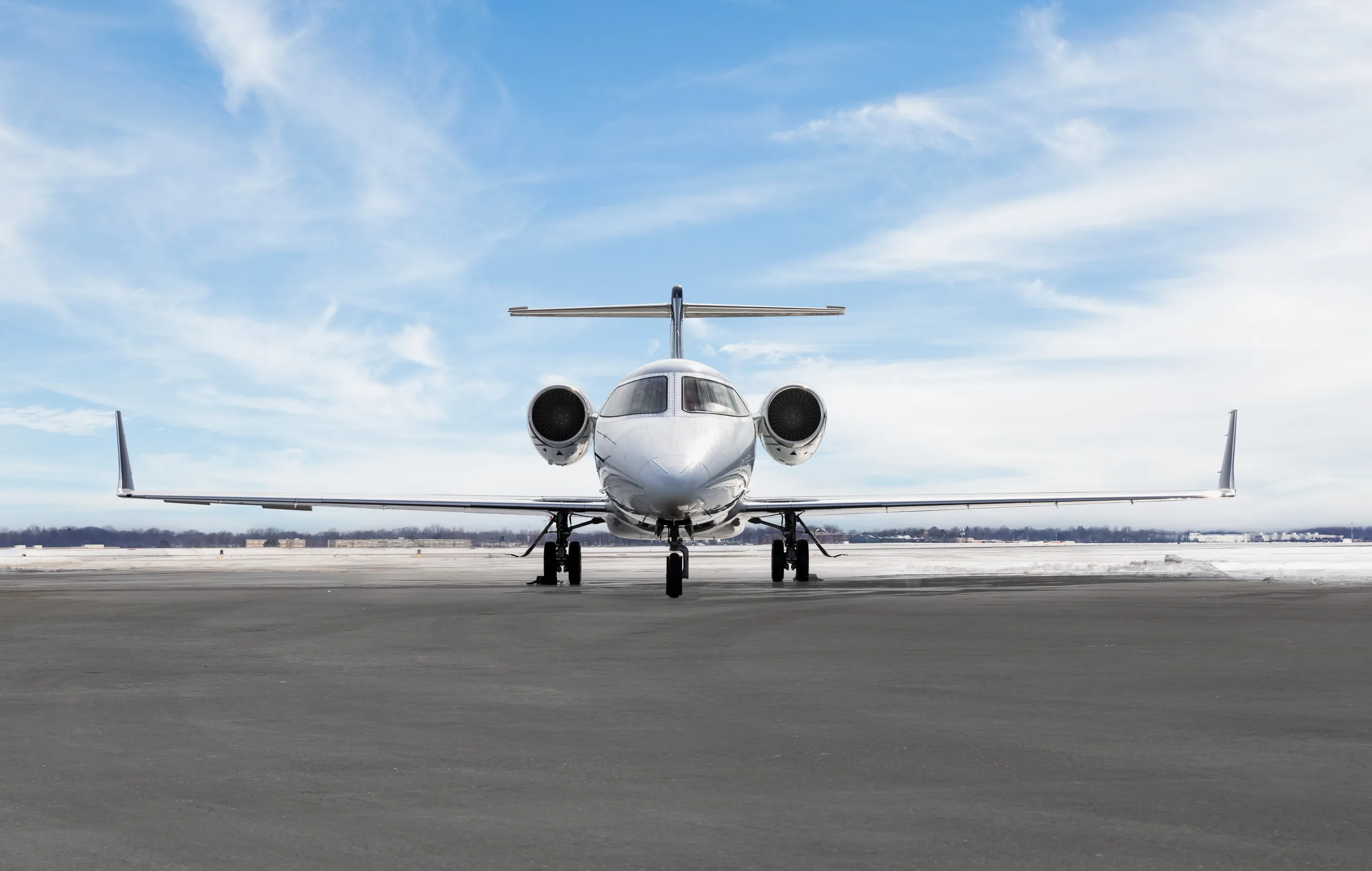 A white Learjet 60 with blue and grey stripes seen from the front, parked on a snowy tarmac.