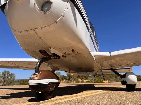 Low angle view of the nose and landing gear of the white and brown aircraft.