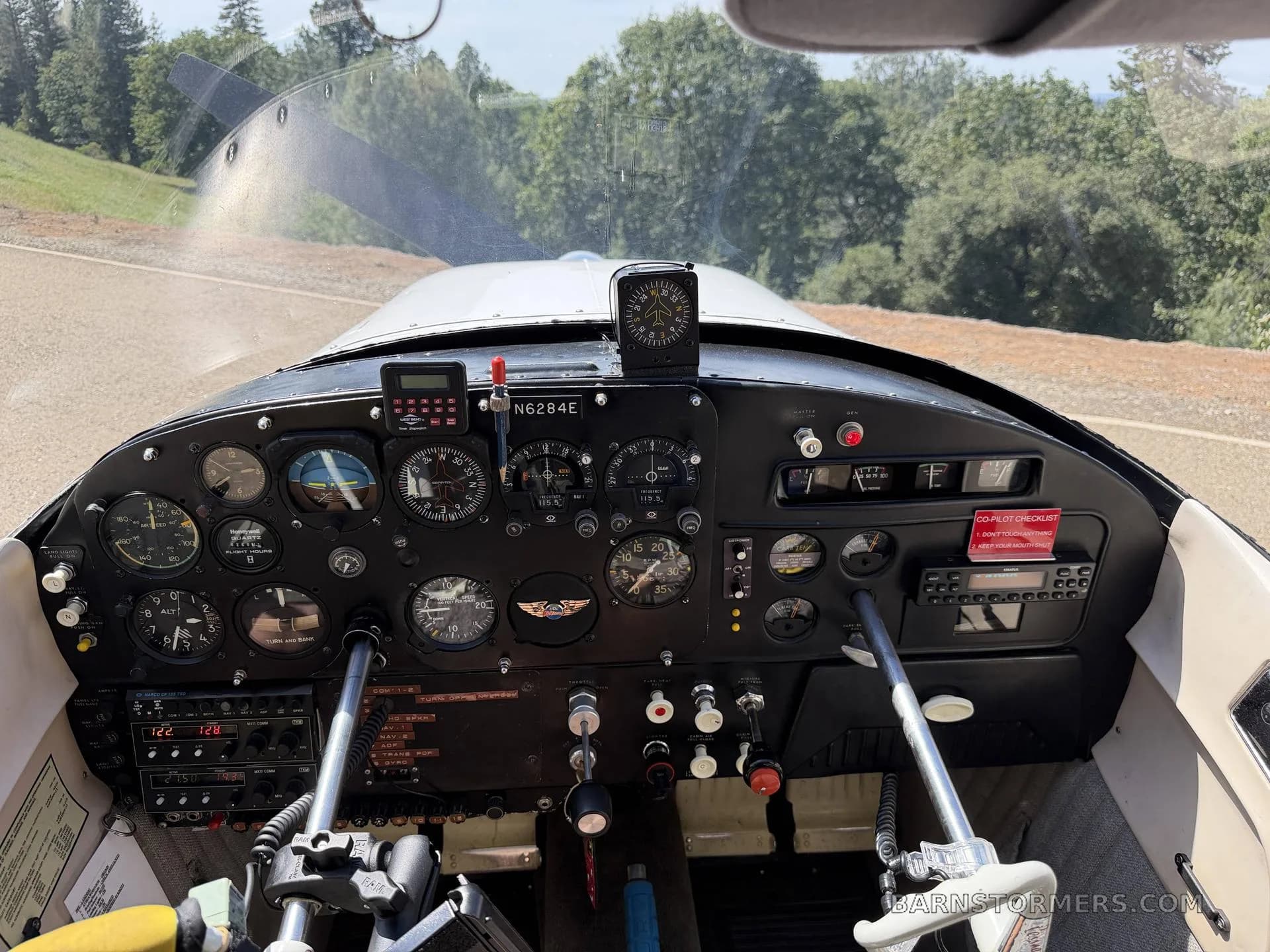 The cockpit of aircraft N6284E, showing the instrument panel and controls, with a view out the windshield to a runway and trees.