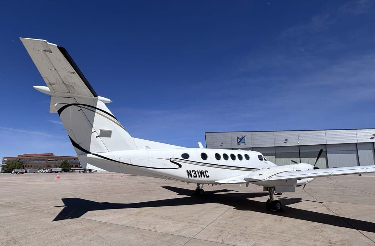 Rear-side view of the white Beechcraft King Air N31WC showing the tail and fuselage with black and gold stripes.