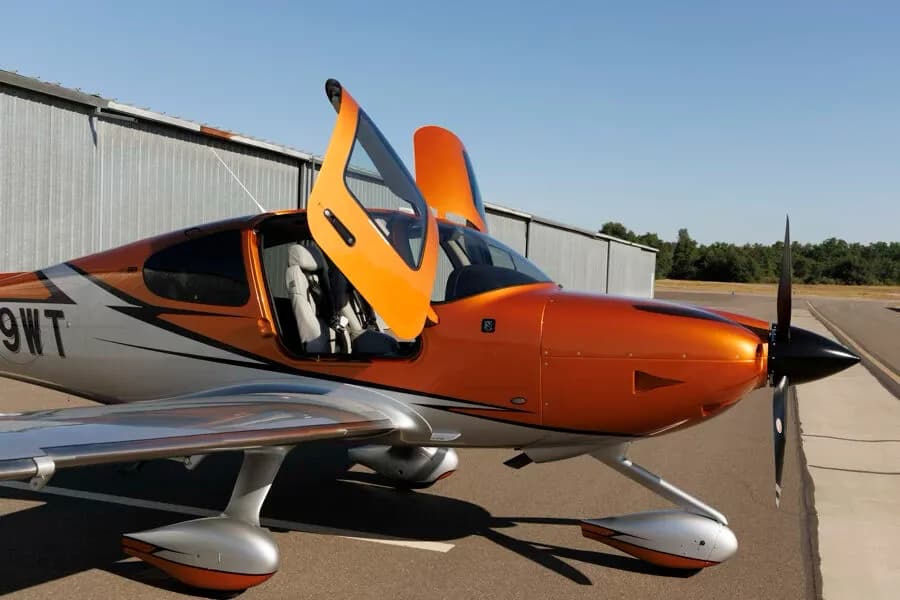 Close-up front-side view of an orange and silver Cirrus SR22T GTS aircraft with the pilot's door open.