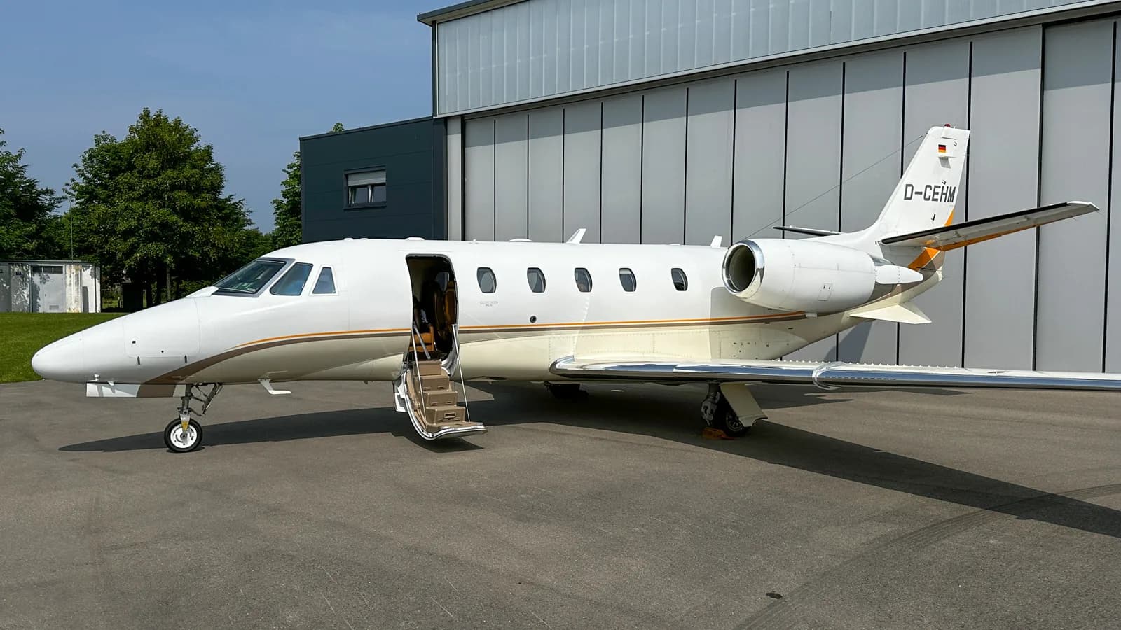 A white Cessna Citation private jet with registration D-CEHM has its cabin door open with stairs extended, parked by a hangar.