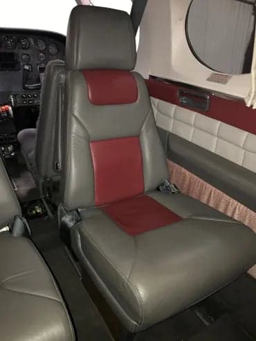 The interior of the aircraft features gray and maroon leather seats with the cockpit visible in the background.