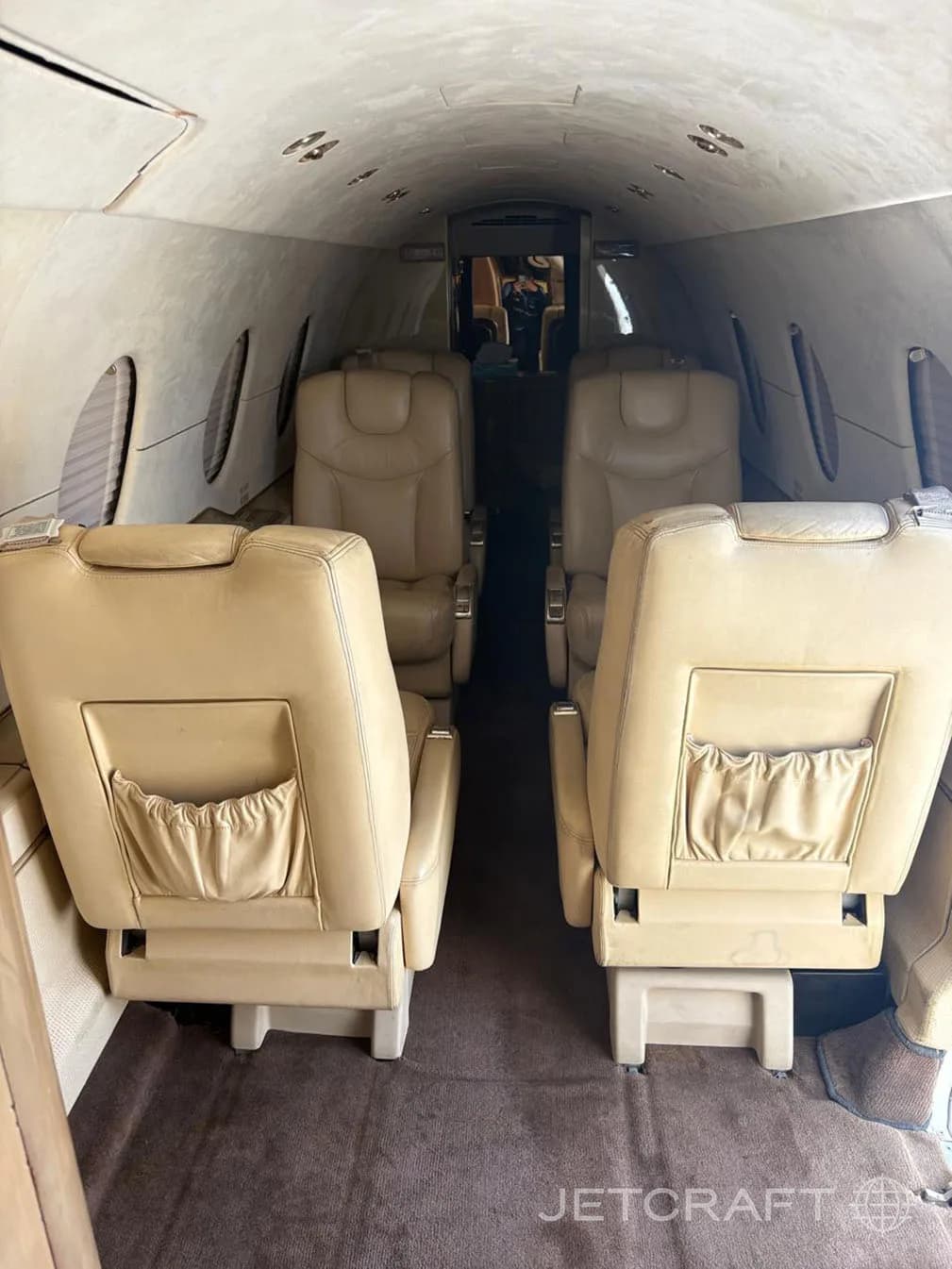 The interior cabin of a private jet with tan leather seats facing forward and aft.