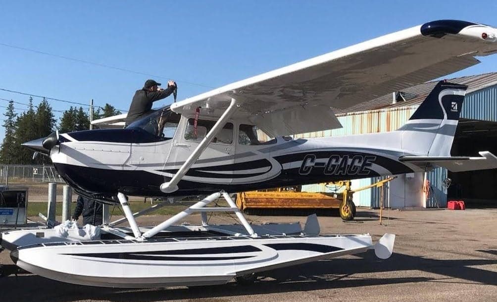A Cessna floatplane is parked on the tarmac with a person on the wing.