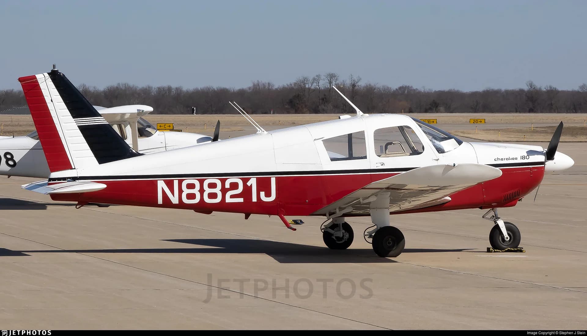 A white and red Piper Cherokee 180 is parked on the tarmac.