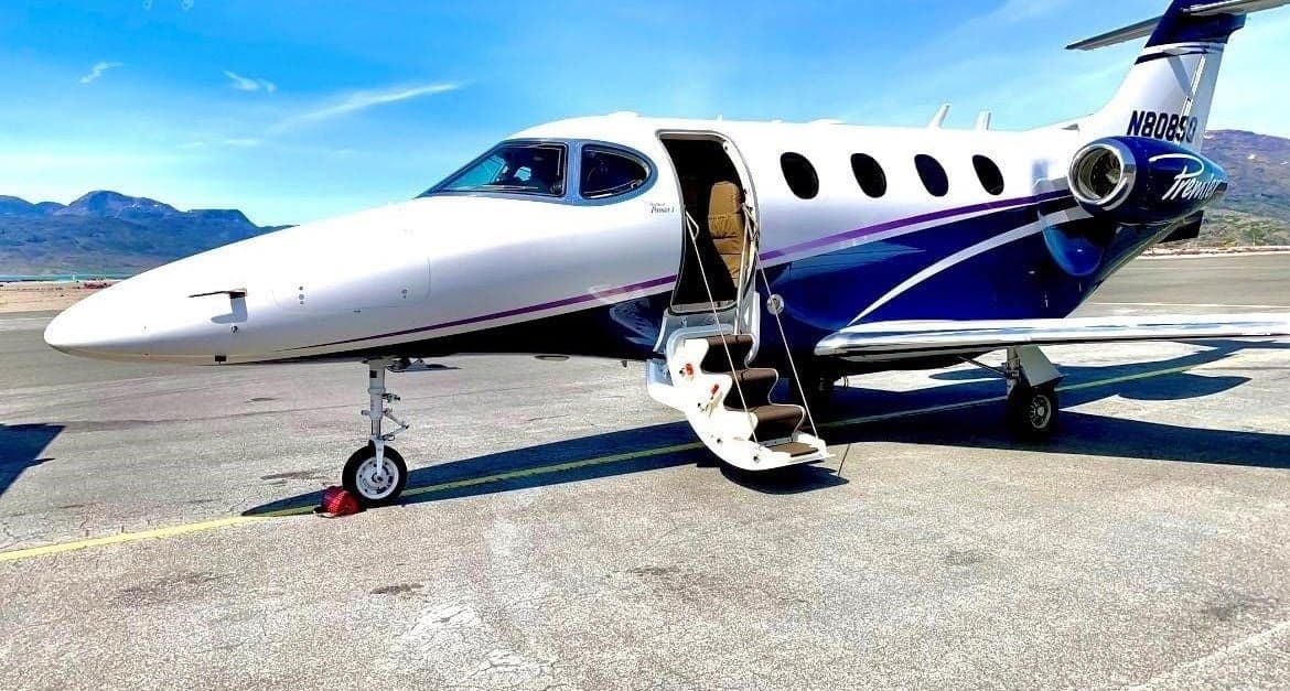 A front-quarter view of a white and blue Beechcraft Premier 1A jet with registration N808SQ, parked on an tarmac with its passenger door open.