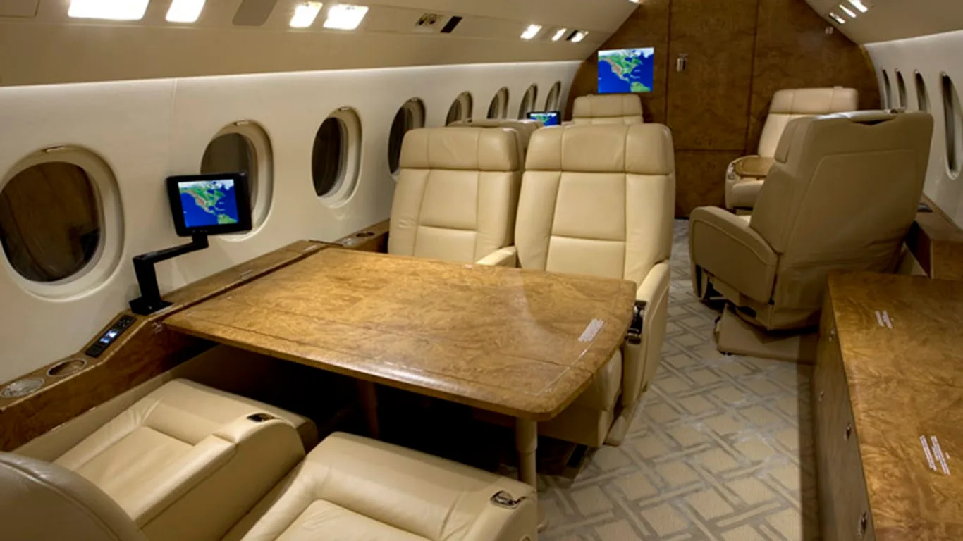 Another view of the aircraft's luxurious cabin, showing beige leather seats, a wooden table, and windows.