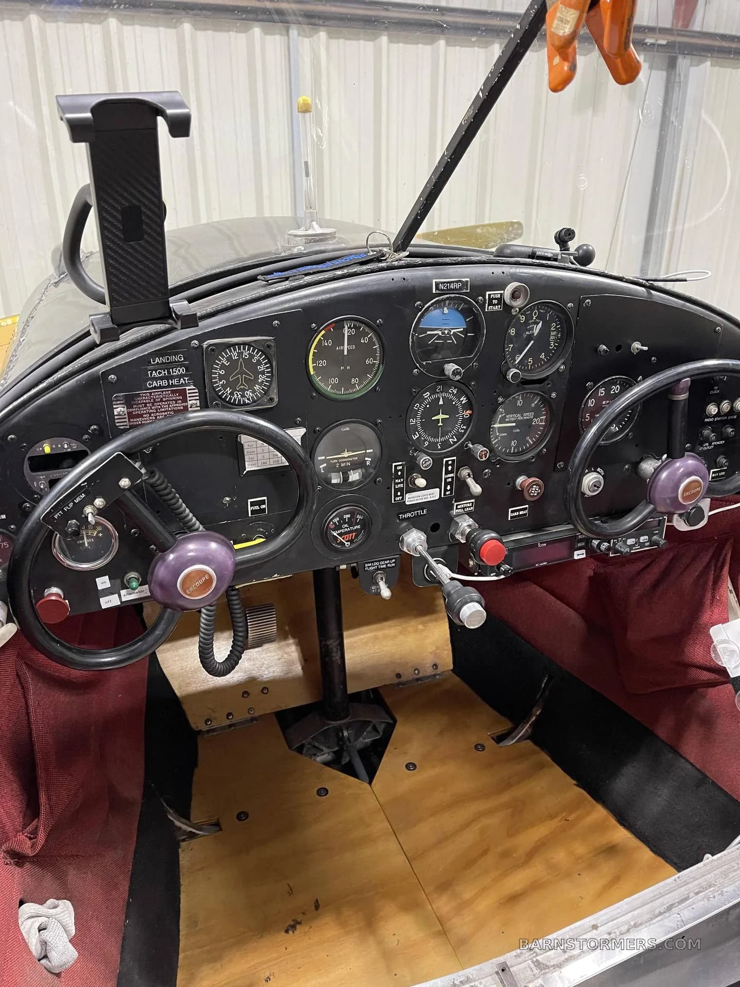 The cockpit of a black and yellow aircraft, featuring a dual control yoke, various gauges, and wooden floorboards.