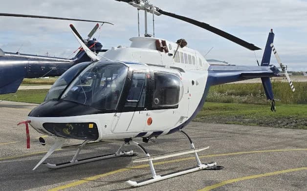 A Bell 206 helicopter in a white and blue paint scheme is parked on the tarmac.