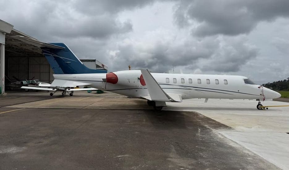 Side view of a white Learjet with blue tail in front of a hangar.