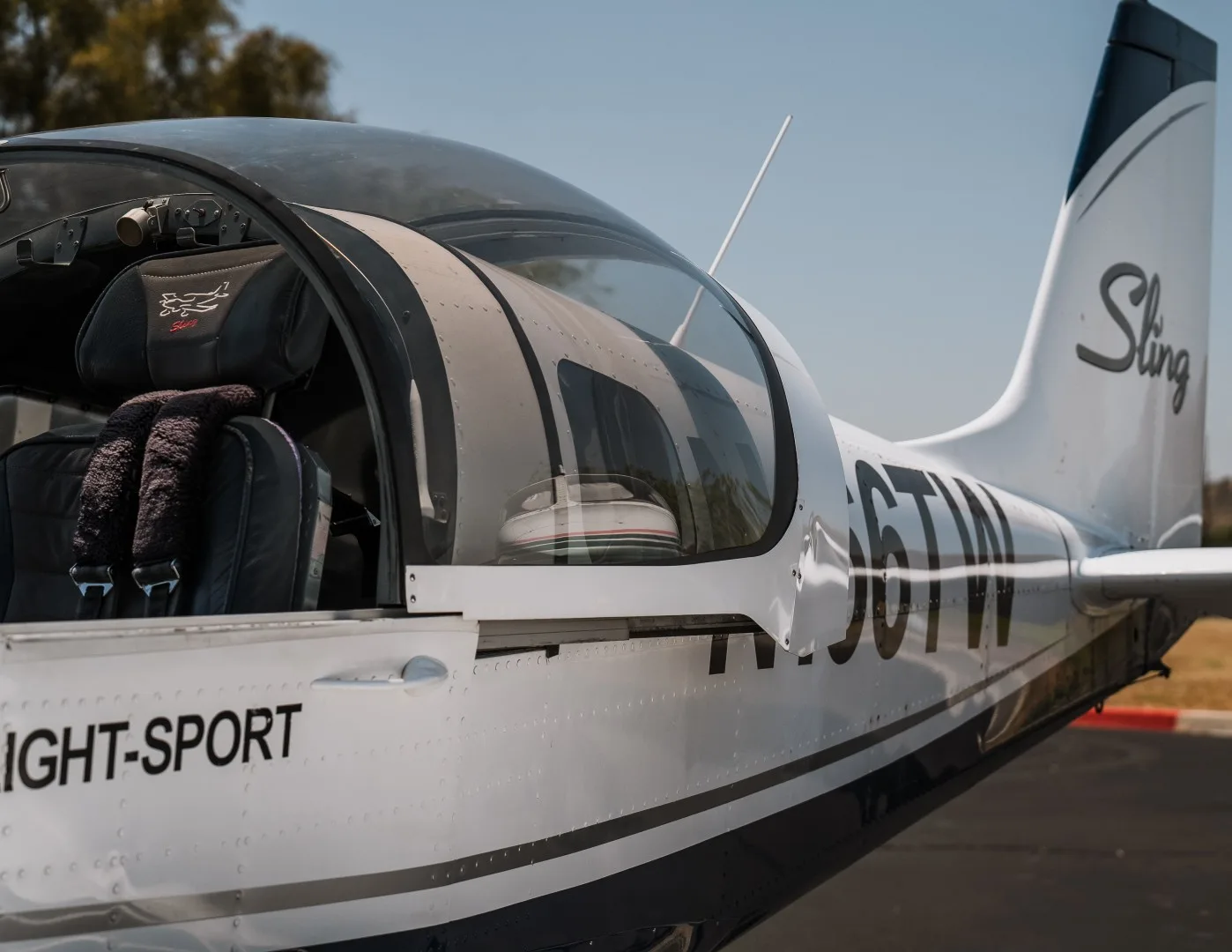 A close-up view of the cockpit and fuselage of the white and blue Sling Light-Sport aircraft, N166TW, with the canopy open.
