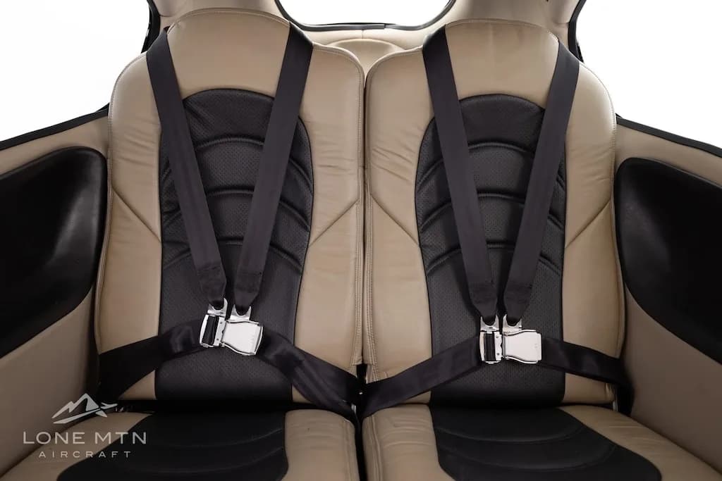 Close-up, straight-on view of two tan and black aircraft seats with harnesses in the cabin.