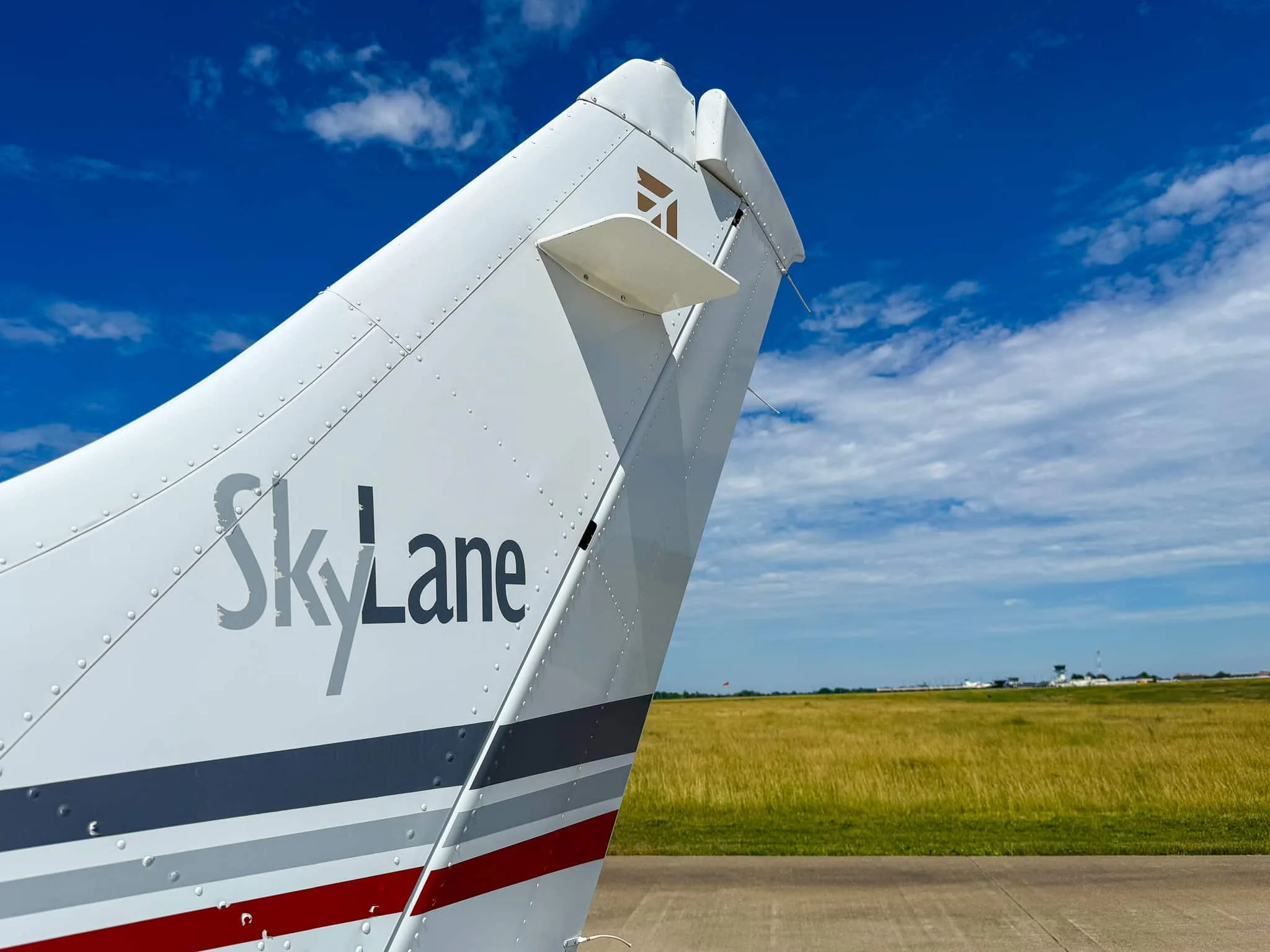 Close-up of the tail of a white Cessna 182 Skylane, showing "SkyLane" text and red and gray stripes.