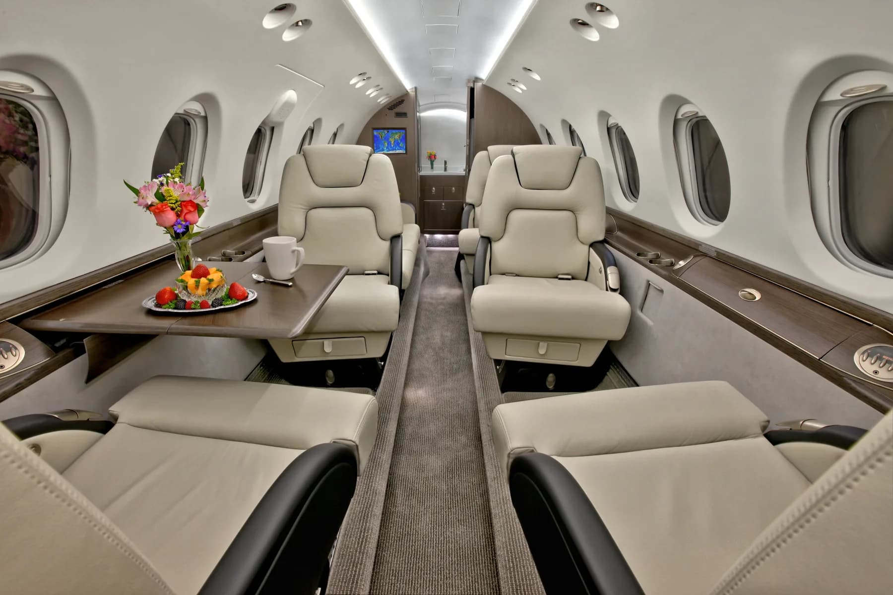 View of the aircraft's interior cabin with cream and black leather seats and a table with flowers and fruit.