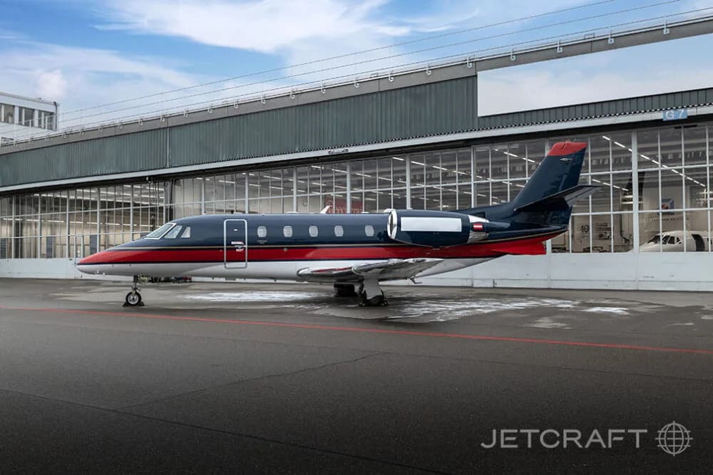 A dark blue, red, and white business jet parked on an asphalt apron in front of a hangar.