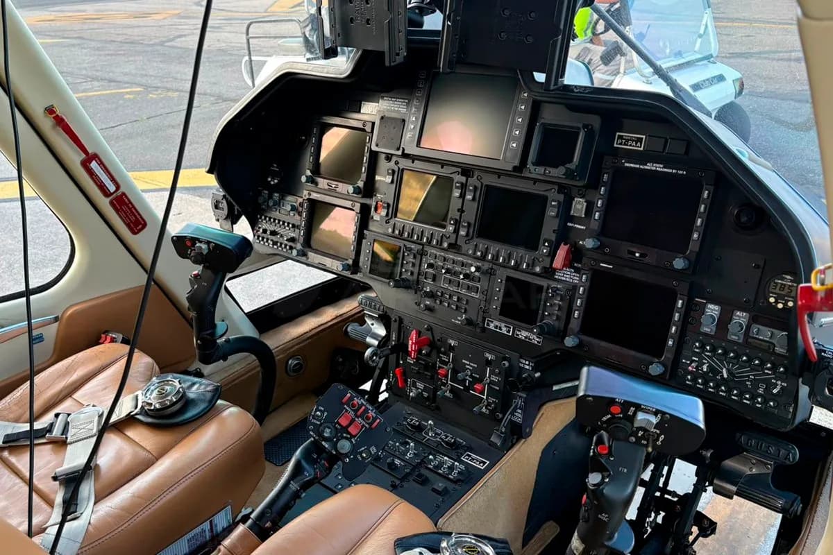 The cockpit of a helicopter showing multiple display screens, controls, and brown leather seats.