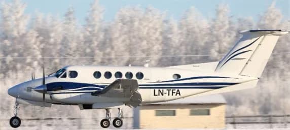 A white and blue turboprop aircraft with registration LN-TFA is seen taking off or landing on a snowy runway with frosted trees in the background.