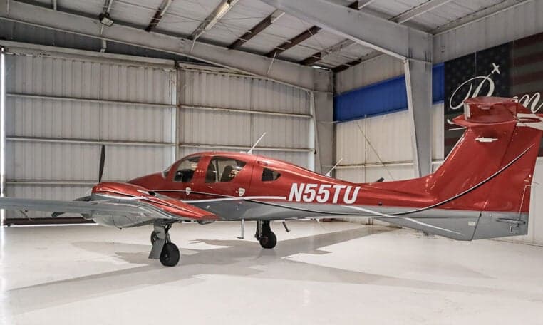 Diamond DA62 aircraft with red and gray paint scheme inside a hangar.