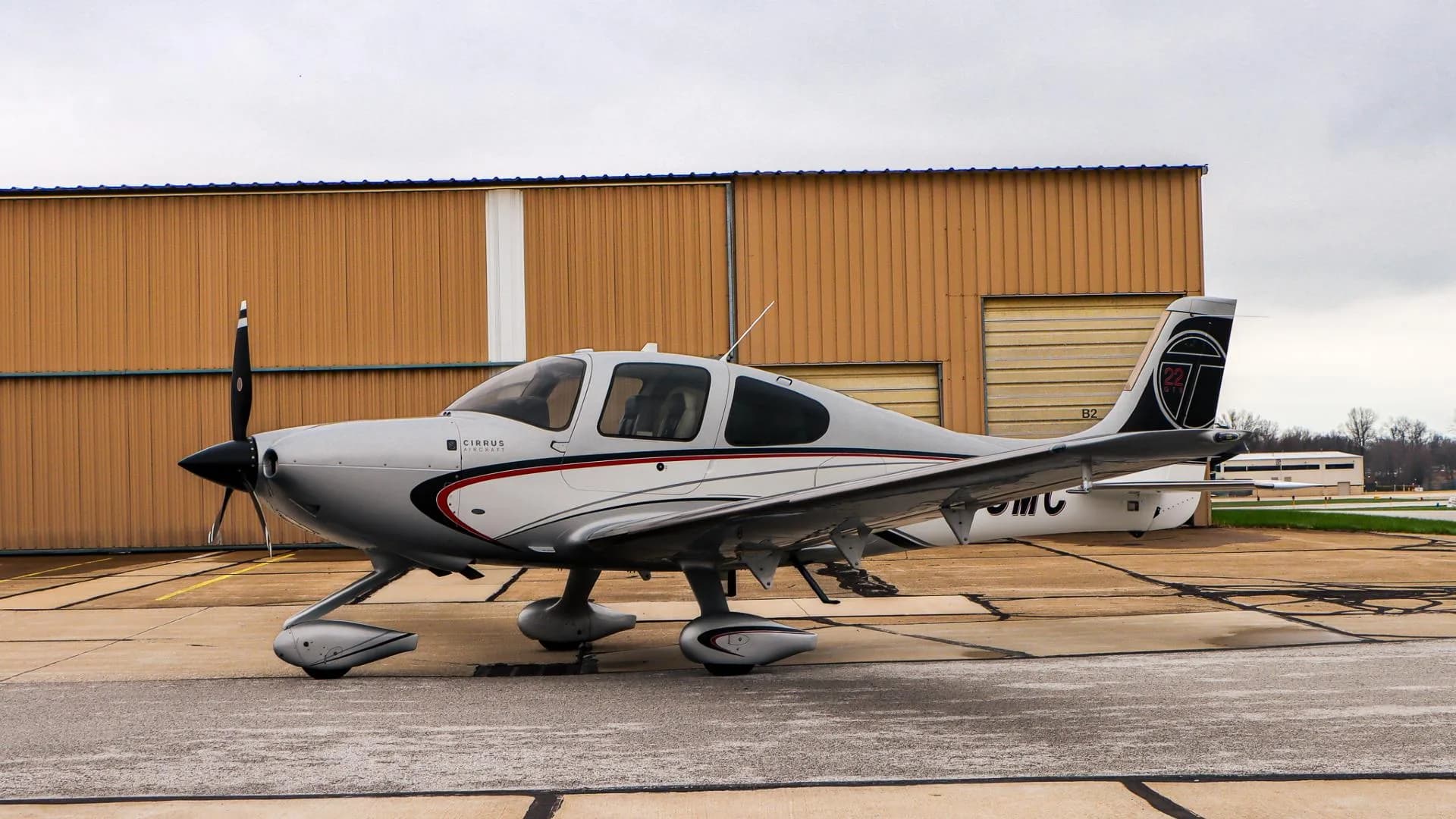 A left side view of the Cirrus SR22 N553MC, parked on an airport tarmac in front of hangars.