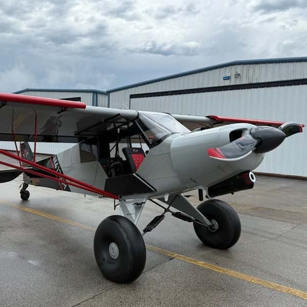 A gray and red N413SM aircraft is parked on the tarmac in front of a hangar on a cloudy day.