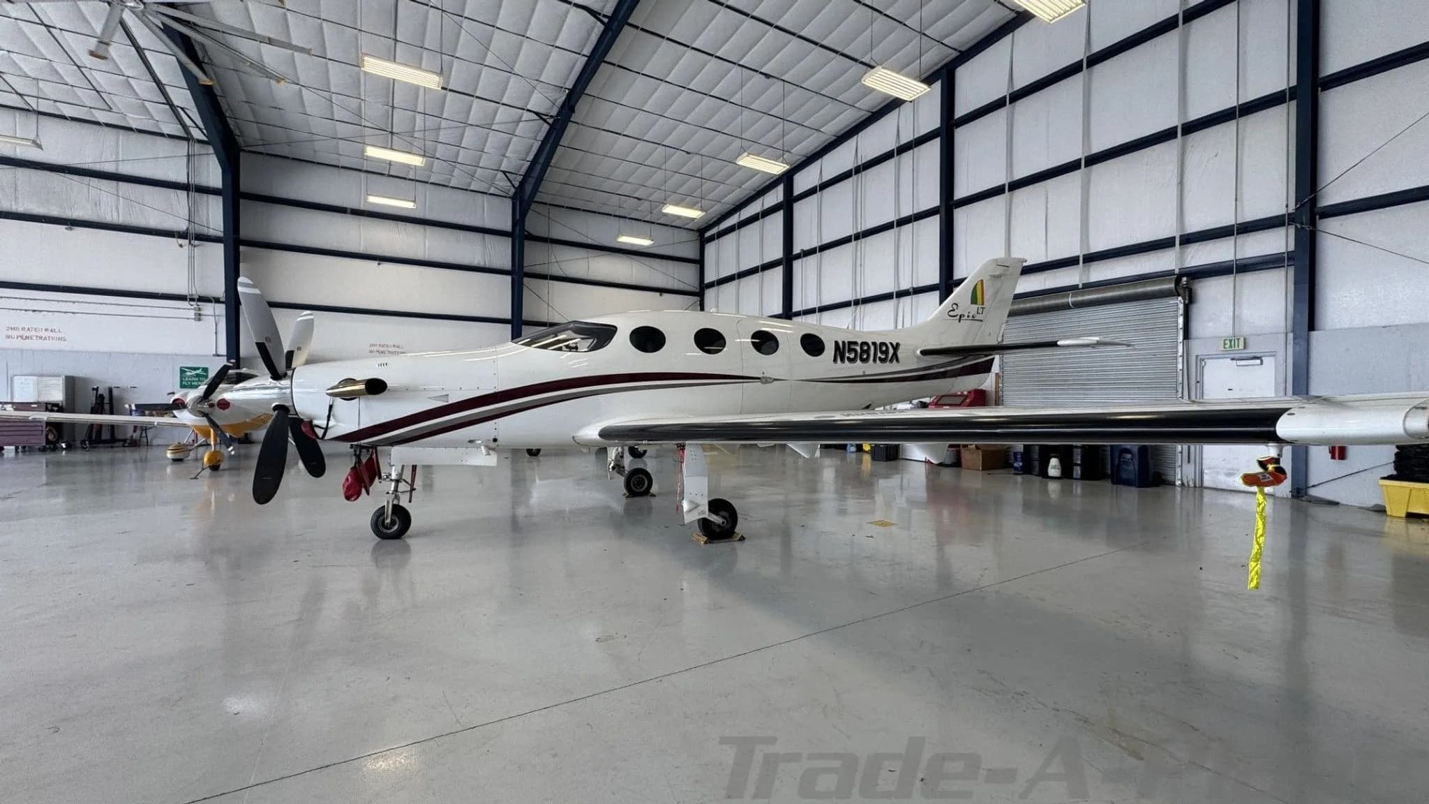 Side view of a white Epic LT aircraft with a dark red stripe and N5819X registration, parked in a hangar.