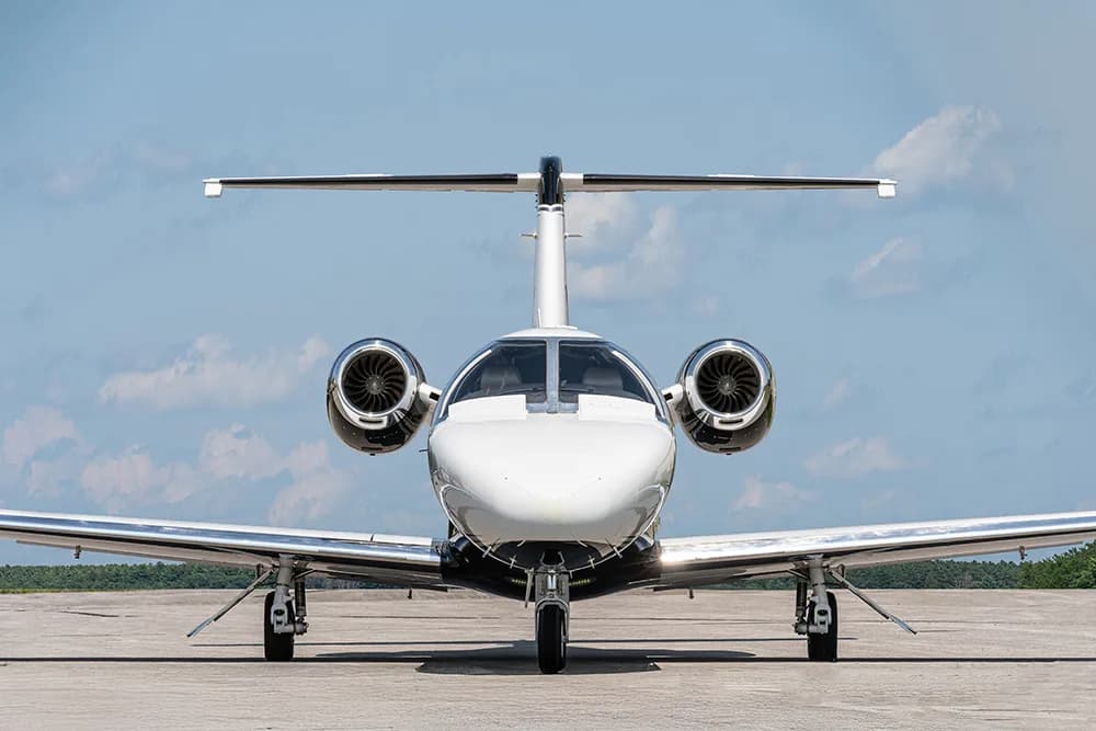 A head-on view of a white and black Citation M2 business jet parked on an airfield.